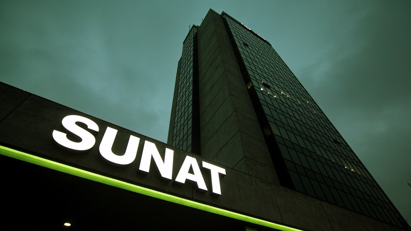 La torre de la SUNAT en Lima al anochecer, con el letrero iluminado en primer plano.